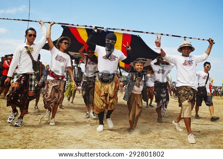 BALI, INDONESIA - 2012 JULY 15: Unidentified young men with joyful faces carrying a huge kite to launch during annual Balinese people festival of traditional kites on the beach Galak in Bali island