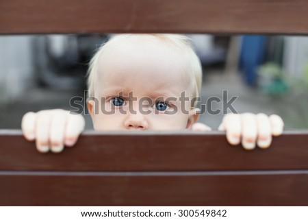 Portrait of abandoned by parents baby boy with staring blue eyes, sad and lonely face expression, looking out through fence. Social problems, family abuse, children stress and negative emotions