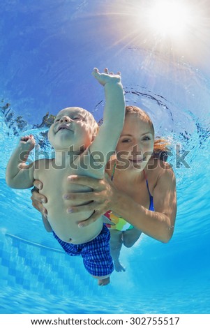 Happy family - positive mother with baby boy swim underwater and dive with fun in blue outdoor pool. Healthy lifestyle, active parents and people water sports activity on summer holidays with children