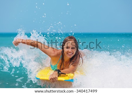 Joyful young girl - beginner surfer with bodyboard has fun on small sea waves. Active family lifestyle, people outdoor water sport lesson and swimming activity on surf camp summer vacation with child