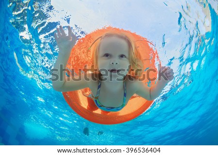 Funny underwater photo of baby girl swimming with fun on orange tube and diving in clear aqua park pool. Healthy family lifestyle, and children water sports activity,  with parents on summer vacation.