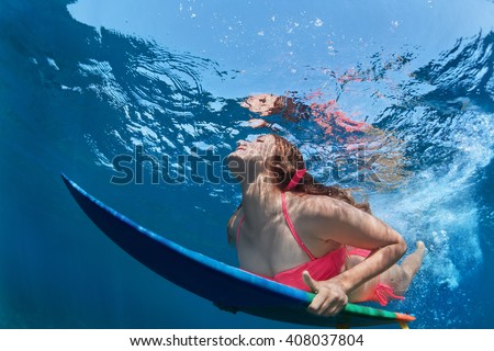 Young girl in bikini in action - surfer with surf board dive underwater with fun under big ocean wave. Family lifestyle, people water sport lessons, beach extreme swimming activity on summer vacation