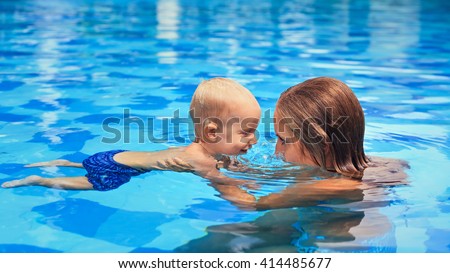 Happy little sports man has swimming lesson with mother - active baby boy swim with fun in woman hands in blue pool. Family lifestyle, summer children water activity and fitness with parents.