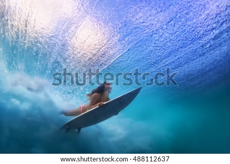 Sportive girl in bikini in action. Surfer with surf board dive underwater under breaking ocean wave. Healthy lifestyle. Water sport, swim and extreme surfing in adventure camp on summer beach vacation