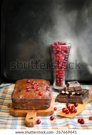 Sweet chocolate pie on a wooden board, with berries and chocolate on a blue-brown checkered cloth and a black background