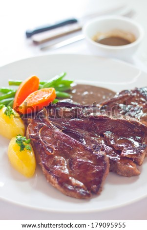 Roasted lamb chops served with fresh carrots, potatoes, beans and brown sauce on big white plate.