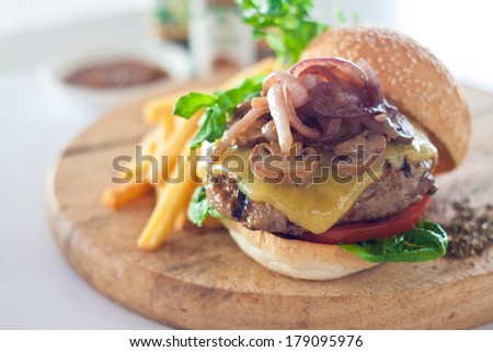 Big mouth cheese burger served with french fries on wooden cutting board.