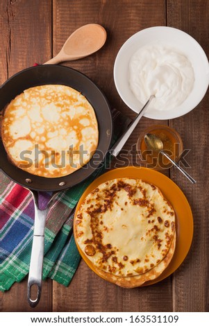homemade pancakes on a frying pan with sour cream and honey on wood table
