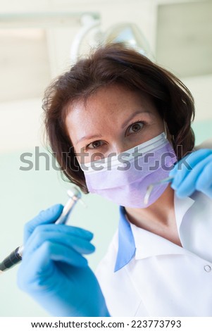 Portrait of woman dentist wearing surgical mask while holding angled mirror and drill selective focus