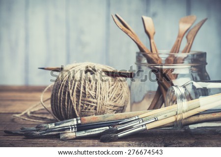 Art and craft tools. Artist\'s brushes, sculpturing set and pencil in glass jars on rustic background. Selective focus.