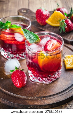 Sangria with oranges, strawberries, mint and ice served in glasses on rustic wooden background. Selective focus.