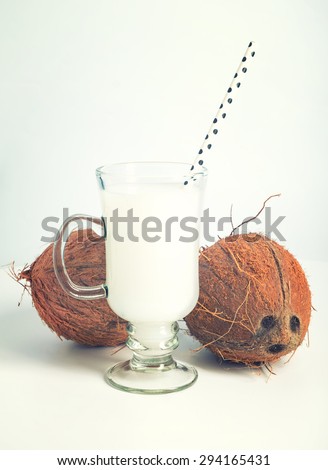Glass of fresh coconut milk with coconuts on back. Warm toning.