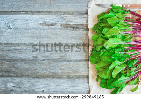 Young fresh beet roots leaves on cutting board, crumpled craft paper and rustic wooden  background close up. Selective focus.