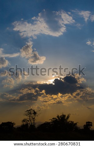 Colorful sunlight sunset behind beautiful clouds and blue sky with shadow and silhouettes of trees and mountains