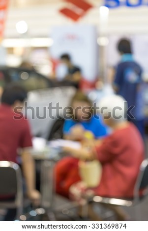 Blurry people meet at commercially cars stand in car shop