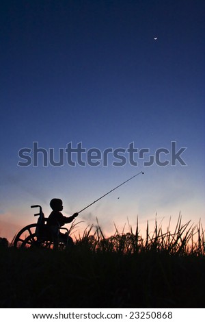 Silhouette of boy in wheel chair fishing at sunset