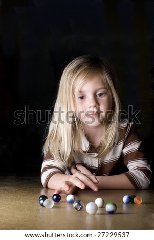 Young girl playing marbles on concrete floor.