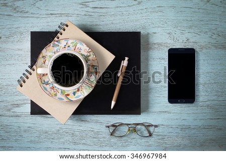 Coffee cup, pen, glasses resting on a mobile phone book on the desk top.