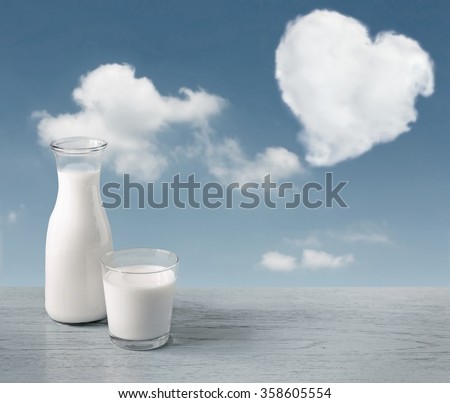 glass of milk and a milk bottle on a wooden table background, sky, clouds heart.