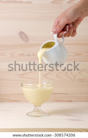 Female hand pouring condensed milk on a light wooden background