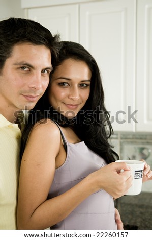An attractive couple enjoys the morning with a kiss and a hot cup of coffee or tea.
