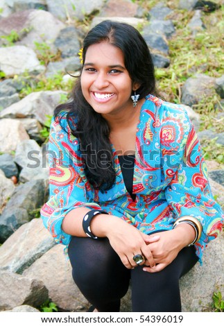 A young and beautiful pakistani model sitting on rocky ground having a bright smile on her face