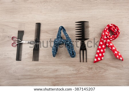 Word hair consist of hairdressing accessories laying on wooden table. Comb, Brush, scissors and colored ribbons