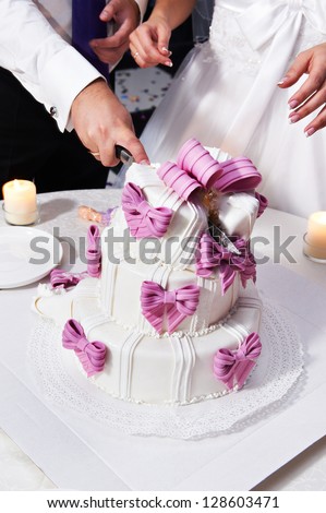 Groom cut the wedding cake with pink bows on solemn banquet
