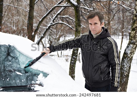 Driver with a brush cleans the car from the snow in the winter