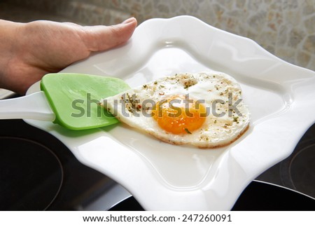 Cook puts fried eggs in the form of heart on a white plate