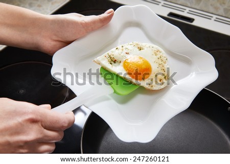 Cook puts fried eggs in the form of heart on a white plate