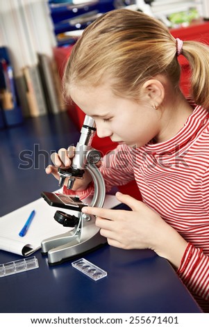 Girl looking through a microscope at home learning table