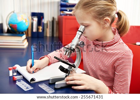 Girl uses a microscope and writes results at home learning table