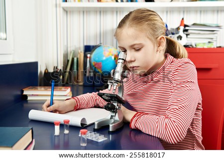 Girl uses a microscope and writes results at home learning table