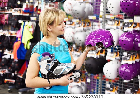 Girl chooses helmet for roller skating in sport shop