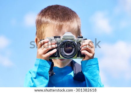 Little boy with retro SLR camera shooting on blue sky