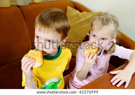 The brother and sister hold crackers and attentively watch TV