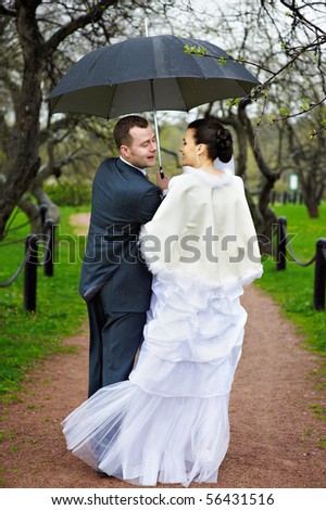 Happy bride and groom at wedding walk with umbrellas in the rain