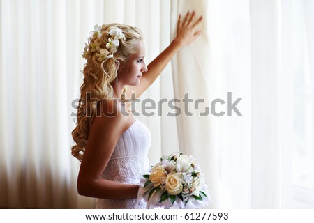 stock photo Happy bride in wedding dress with flowers near sunny window