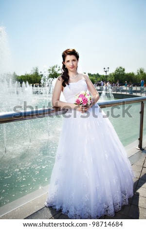 Happy bride about fountain with bouquet at wedding walk in the park