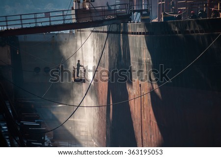 Shipyard worker power washing a ship on dry dock.