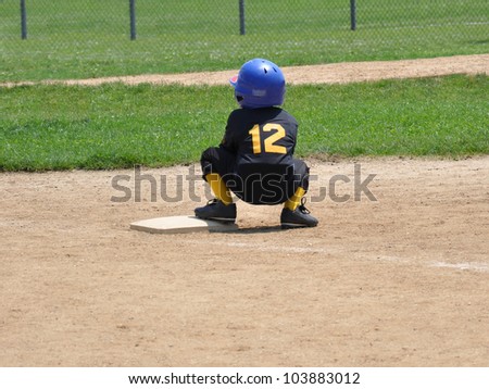 School Age Child Squatting on Baseball field Base wearing uniform number 12 and blue helmet