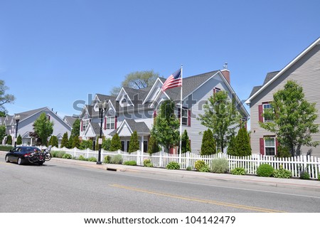 Suburban Street American Flag Row Town Houses Car passing with Bicycles mounted on trunk sunny blue sky day
