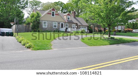 Half Circle Blacktop Driveway Suburban Stone Home in Residential Neighborhood along street with double yellow traffic dividing lines