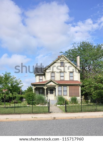 Victorian Home with black rod iron fence in suburban neighborhood sunny blue sky day
