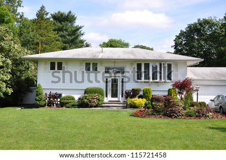 Suburban High Ranch Style Home Landscaped with flowers plants shrubs bushes sunny blue sky day