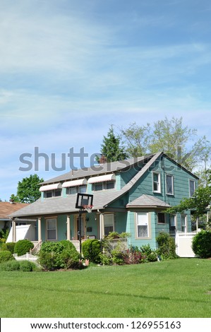 Suburban Neighborhood Cape Code Style Home with Basketball Hoop on Landscaped Front Yard Lawn Sunny Blue Sky Day