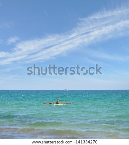 Woman Kayaking in Mediterranean Sea Beautiful Blue Sky with Clouds Streaming Across passing Sailboat in distant background