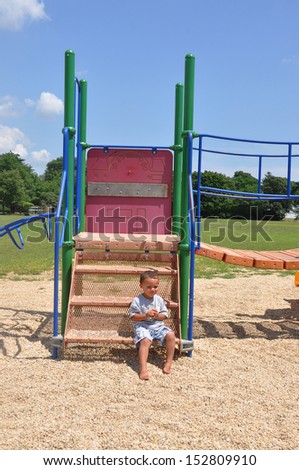 Handsome Toddler Boy sitting Thinking on Playground Equipment Sunny Blue Sky Day Suburban Residential Neighborhood