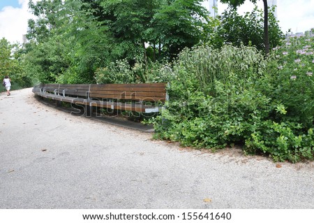 Woman Walking along Brooklyn Bridge Path lined with plants and wood bench
